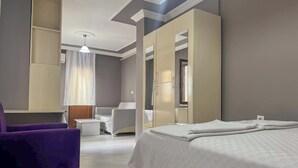 A modern hotel room with a bed, a seating area with a purple chair, a small table, and a wardrobe. - Kalmuk Suite Hotel (Trabzon)