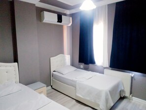 A hotel room with a single bed, a bedside table, an air conditioning unit, and a window with curtains. - Kalmuk Suite Hotel (Trabzon)