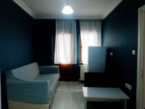 A small, dimly lit room with a blue wall, a white radiator, a blue sofa, and a small table. - Kalmuk Suite Hotel (Trabzon)