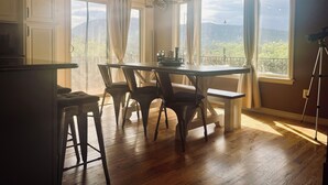 A kitchen with a wooden table and chairs, large windows with curtains, and a tripod on the floor. - Entire home in Palmer Lake, CO (Palmer Lake)