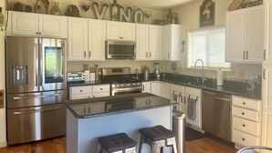 A modern kitchen with white cabinets, stainless steel appliances, and a central island with stools. - Entire home in Palmer Lake, CO (Palmer Lake)