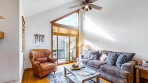 A living room with a leather armchair, a grey sofa, a coffee table, and a ceiling fan. - Ski In, Ski Out 3 Bedroom Townhome at Snowflake Lift - Private Hot Tub (Breckenridge)