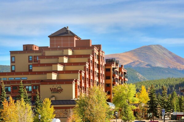 Un hotel de varios pisos con un letrero grande de Village, rodeado de árboles y una montaña al fondo.
