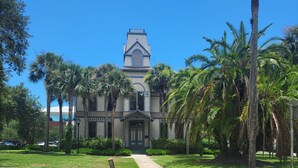 A building with a prominent tower and a symmetrical facade, surrounded by palm trees and a well-maintained lawn. - Charming 1925 House in the Heart of DeLand.  (DeLand)