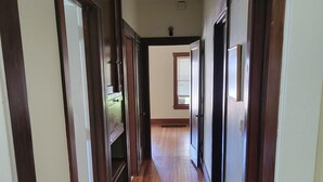 A hallway with wooden floors and doors, leading to a room with a window and blinds. - Charming 1925 House in the Heart of DeLand.  (DeLand)