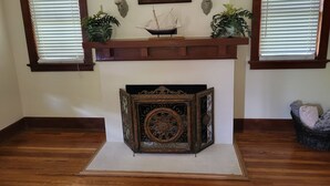 A room with a fireplace, a framed picture above it, and two windows with blinds. - Charming 1925 House in the Heart of DeLand.  (DeLand)