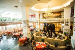 A hotel lobby with a central fountain, multiple dining tables, and a chandelier. - Jin Yuan Holiday Hotel (Shantou)