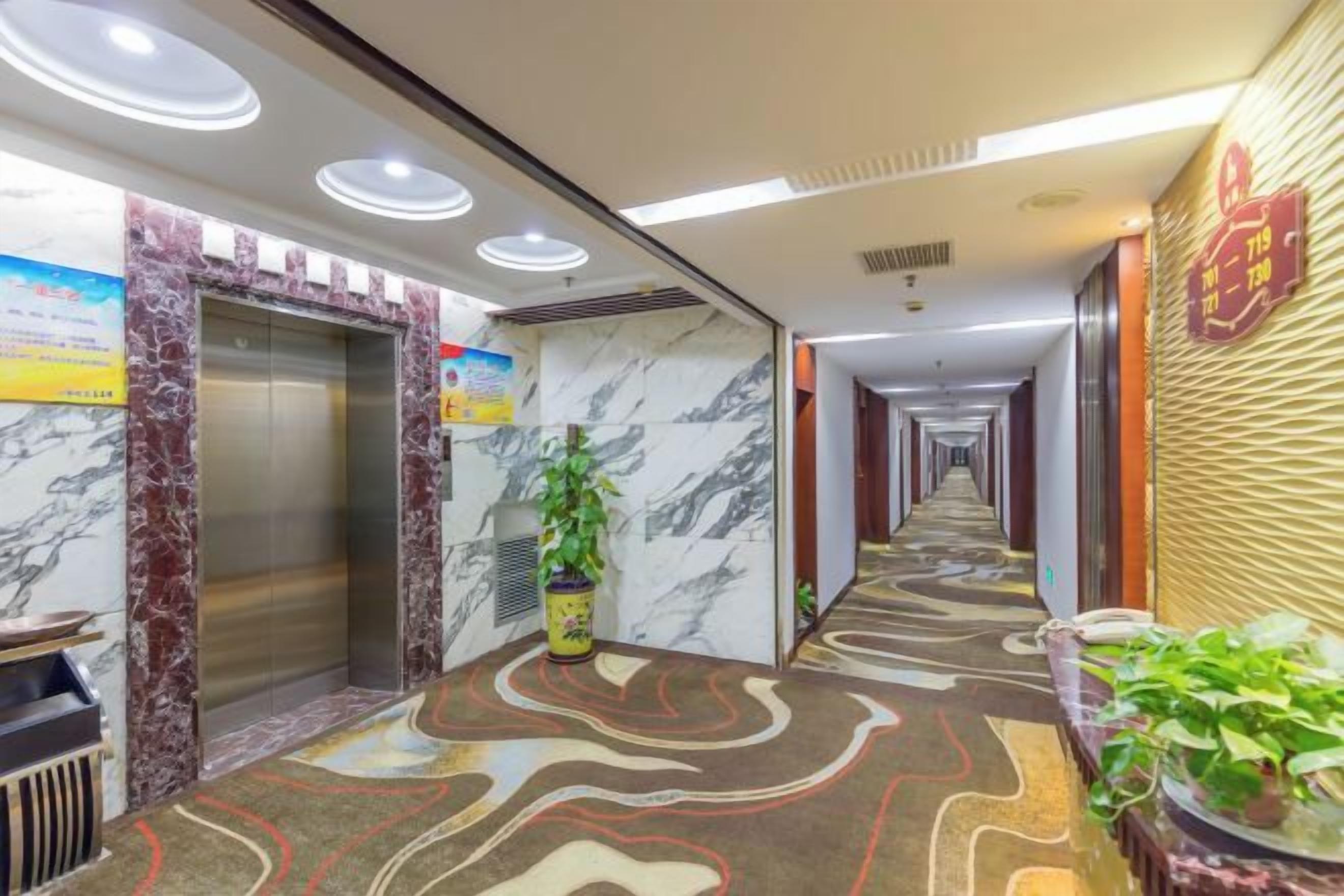 Pasillo de hotel con paredes de mármol, un ascensor y una alfombra estampada.