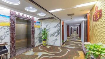 Pasillo de hotel con paredes de mármol, un ascensor y una alfombra estampada.