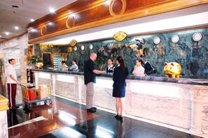 Un hall d’accueil d’hôtel avec un comptoir en marbre, un bureau d’accueil et une décoration en forme de tirelire dorée.