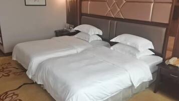 Een hotelkamer met twee bedden, een hoofdbord met een geometrisch patroon, een nachtkastje met een lamp en een vloerkleed met bloemenmotief.