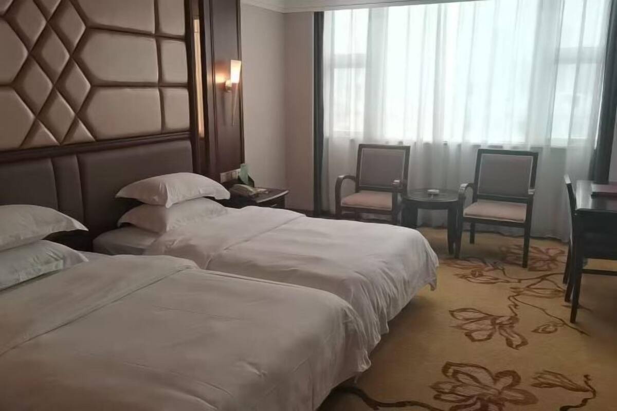Een hotelkamer met twee bedden, een bureau, stoelen, een tafeltje en een raam met gordijnen.
