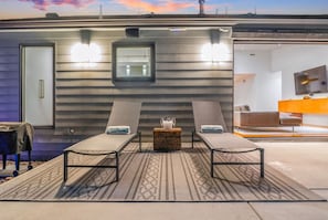 A modern outdoor lounge area with two sun loungers, a small table with a drink, and a television in the background. - Lux Villa: Heated Pool & Sauna (San Diego)