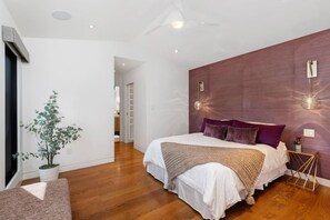 A modern bedroom with a large bed, a potted plant, and a wooden floor.