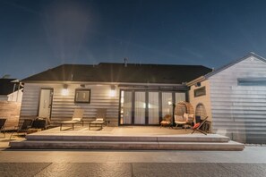 A modern house with a covered patio, outdoor seating, and a large window.