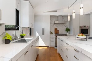 Una cocina moderna con armarios blancos, encimera de mármol, horno integrado e iluminación colgante.