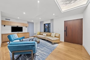 A modern living room with a sofa, a blue armchair, a coffee table, and a TV mounted on the wall. - Lux Villa: Heated Pool & Sauna (San Diego)