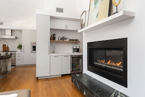 A modern kitchen with white cabinetry, a coffee station, and a black fireplace. - Lux Villa: Heated Pool & Sauna (San Diego)