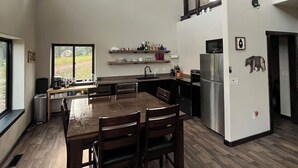A spacious kitchen with a dining area, large windows, and a high ceiling.