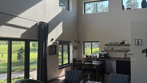 A spacious living area with large windows, a dining table, and a kitchen area.