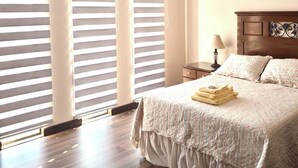 Un dormitorio con una cama grande, piso de madera y una ventana con persianas.