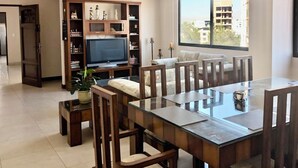 Amplia sala de estar con una gran mesa de comedor, sillas de madera, un televisor y una estantería.