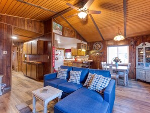 Interior acogedor de una cabaña con un sofá azul, techo de madera y comedor con mesa y sillas.