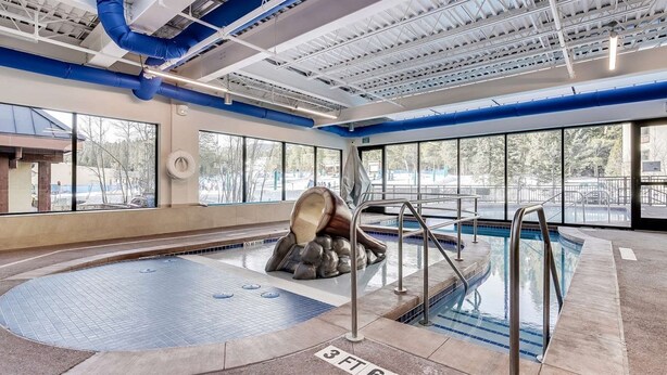 An indoor swimming pool with a large rock sculpture, clear windows, and a blue ceiling. - Comfortable 3-bedroom Ski In/out Condo at Peak 9 - Village at Breckenridge (Breckenridge)