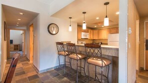 A kitchen with a bar area, wooden cabinets, and a clock on the wall. - Comfortable 3-bedroom Ski In/out Condo at Peak 9 - Village at Breckenridge (Breckenridge)