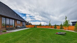 A modern house with a large lawn, a barbecue area, and a wooden fence. - New Modern 5BR with AC - Walk to Targhee Shuttle (Driggs)