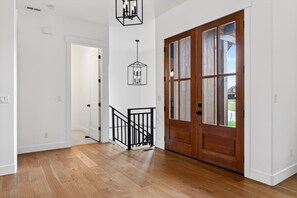 A hallway with wooden flooring, a wooden door with glass panels, and a black railing. - New Modern 5BR with AC - Walk to Targhee Shuttle (Driggs)
