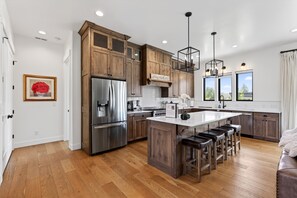 A modern kitchen with wooden cabinets, stainless steel appliances, and a large island with bar stools. - New Modern 5BR with AC - Walk to Targhee Shuttle (Driggs)