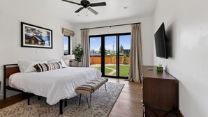 A bedroom with a bed, a desk, a television, a ceiling fan, a window, and a sliding glass door. - New Modern 5BR with AC - Walk to Targhee Shuttle (Driggs)