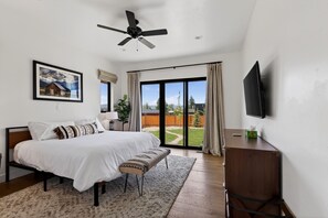 A bedroom with a bed, a desk, a television, a ceiling fan, a window, and a sliding glass door. - New Modern 5BR with AC - Walk to Targhee Shuttle (Driggs)