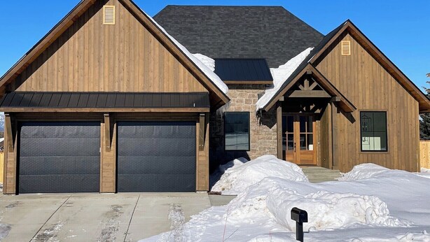 A two-story wooden house with a stone facade, two garage doors, and a snow-covered driveway. - New Modern 5BR with AC - Walk to Targhee Shuttle (Driggs)