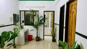 A hallway with a tiled floor, potted plants, a red bucket, and a wooden door. - Green House (Khulna)