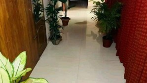 A hallway with potted plants, a wooden door, and a red curtain. - Green House (Khulna)