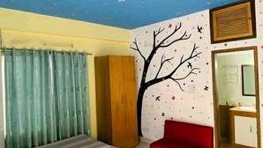 A bedroom with a bed, a wardrobe, a red chair, a wall-mounted radiator, and a mirror. - Green House (Khulna)