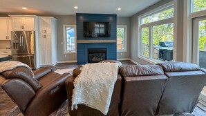 A modern living room with a fireplace, leather sofa, and large windows offering a view of the outdoors. - Escape to a lakeside cabin with stunning panoramic views of Ottertail Lake
 (Ottertail)