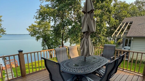 A wooden deck with a round table and chairs, an umbrella, and a view of the water. - Escape to a lakeside cabin with stunning panoramic views of Ottertail Lake
 (Ottertail)