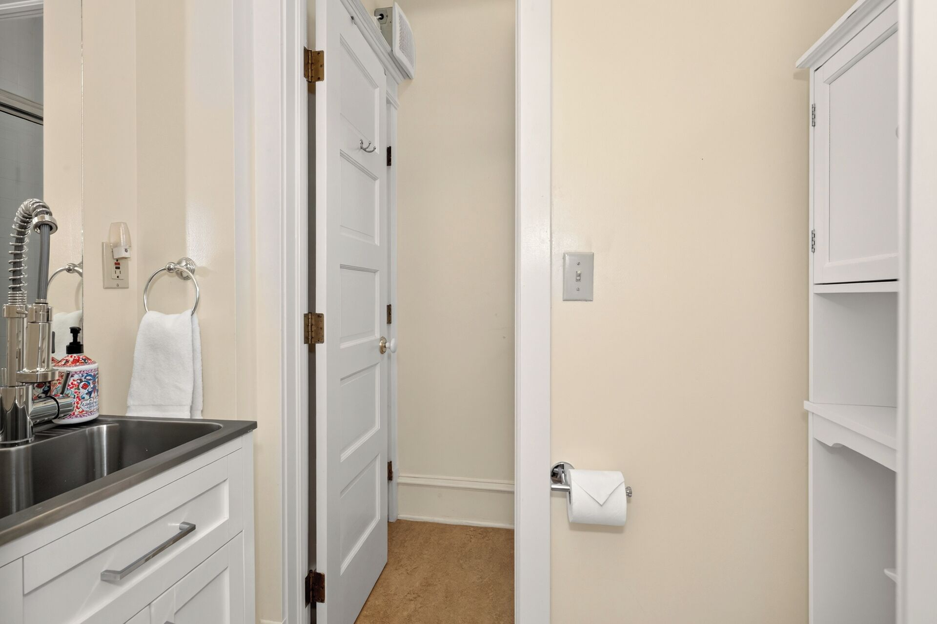 A bathroom with a sink, mirror, towel rack, toilet paper holder, and a door leading to another room.