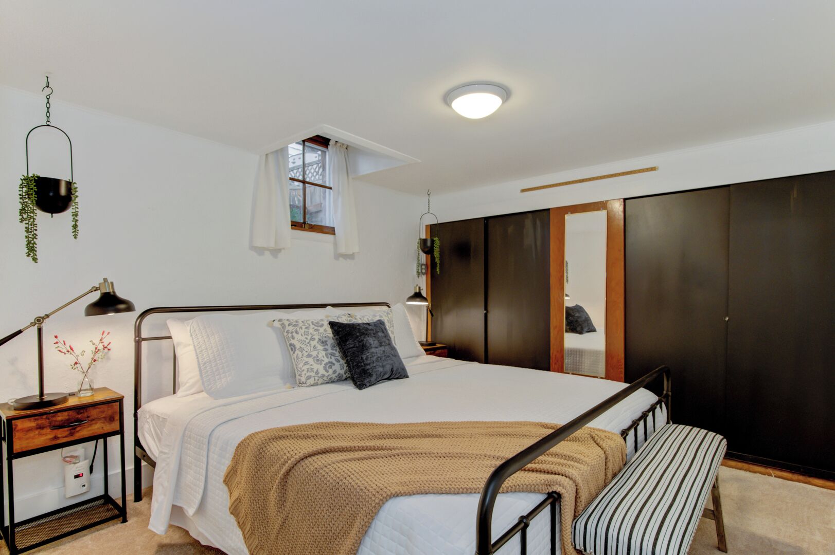 A modern bedroom with a bed, bedside tables, a hanging plant, a window, and a wardrobe.