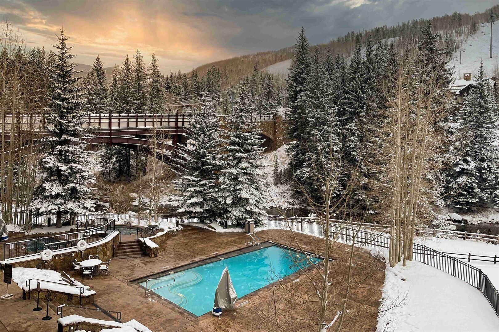 A pool area with a wooden deck, surrounded by snow-covered trees and a mountain backdrop.