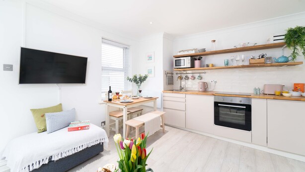 Una cocina moderna con armarios blancos, una encimera de madera y un horno empotrado. Hay una mesa de comedor con sillas y un banco.