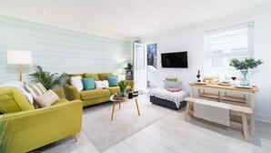 Una sala de estar moderna con un sofá verde, una mesita de centro, un banco y una zona de comedor con una mesa y sillas de madera.