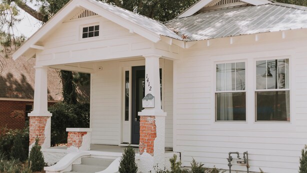 A white single-story house with a front porch, brick columns, and a small front yard.