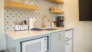 A kitchen with a microwave, sink, and cabinets. There are utensils and a coffee maker on the counter.