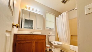 Une salle de bain avec des meubles en bois, des toilettes, un lavabo et une douche avec un rideau.