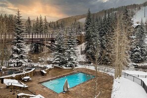 A pool area with a wooden deck, surrounded by snow-covered trees and a mountain backdrop.