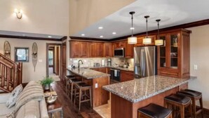 A spacious kitchen with wooden cabinets, granite countertops, and a large island with bar stools. - Ski In, Ski Out 3 Bedroom Condo at the Eagle Bahn Gondola With Slopeside Pool (Vail)